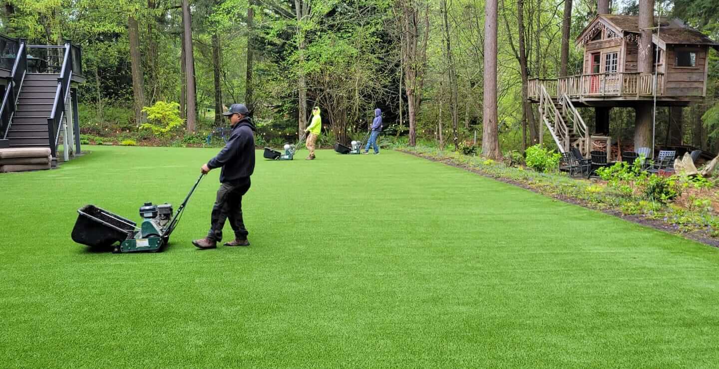 Professional artificial grass installers finishing a backyard lawn installation in the Seattle, Washington area